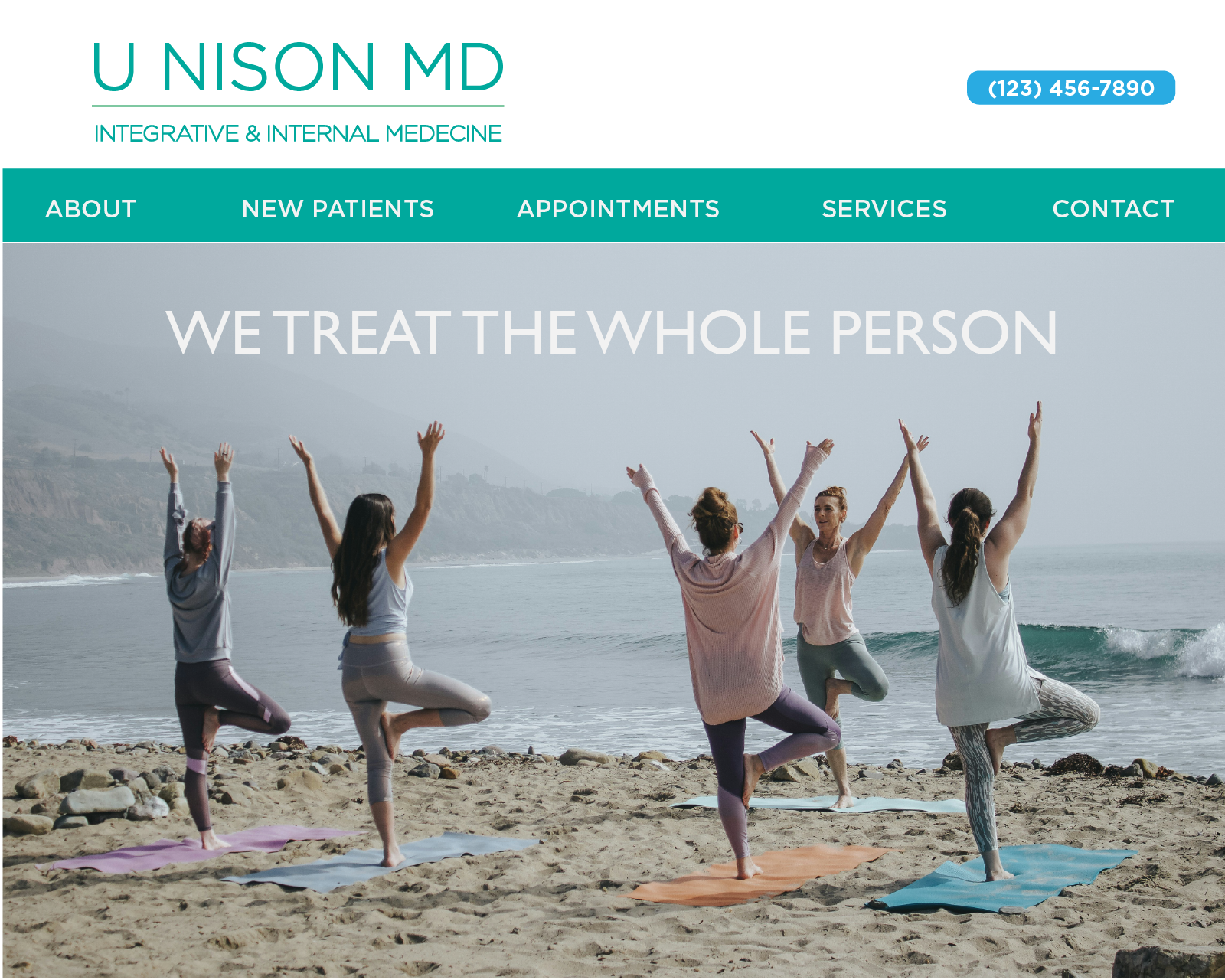 Five women practicing yoga tree pose on mats on a beach with ocean waves and hills in the background.